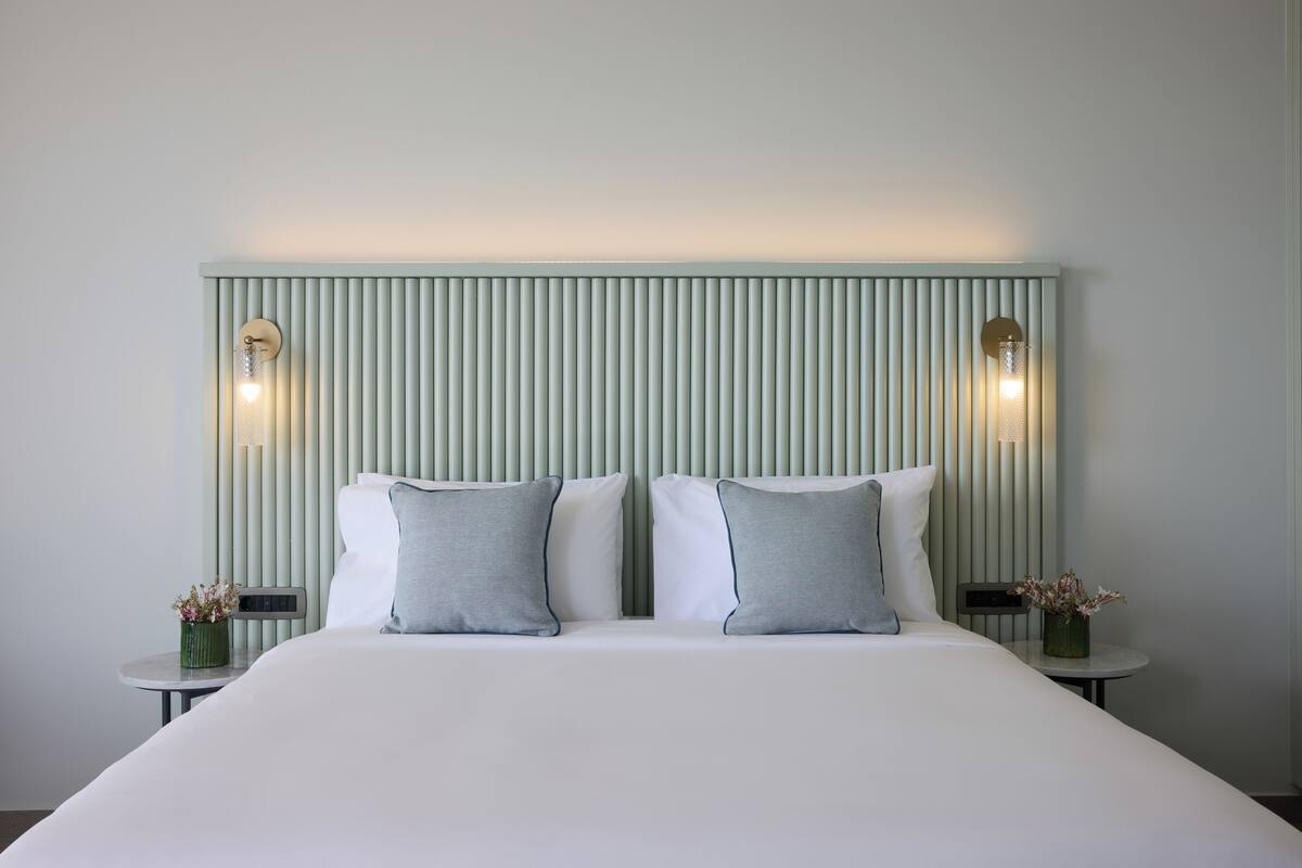 A hotel room with a large bed, two bedside tables, and a wall-mounted light fixture.