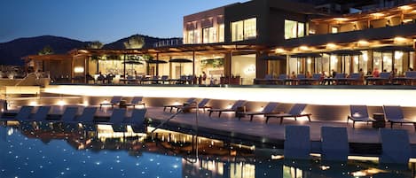 A modern hotel with a pool area, outdoor seating, and a mountain backdrop.