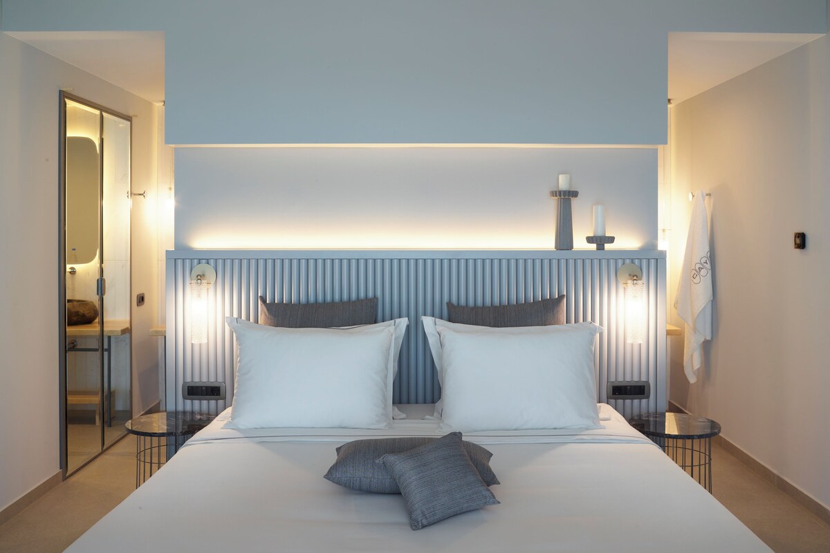 A modern hotel room with a large bed, bedside tables, a nightstand, and a bathroom visible through an open door.