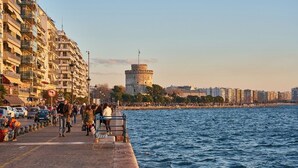 A waterfront promenade with a historic tower, modern buildings, and a busy pedestrian area. - Zennova 9 City Center Pearl (Thessaloniki)