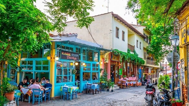 A cobblestone street lined with colorful buildings, outdoor seating at a café, and parked motorcycles. - Zennova 9 City Center Pearl (Thessaloniki)