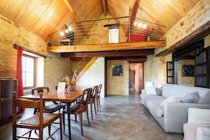 A dining area with a wooden table and chairs, a white sofa, and a loft space with a railing.