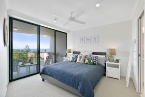 Relax in this serene bedroom with a large bed, nightstands, and a sliding glass door leading to a furnished balcony.