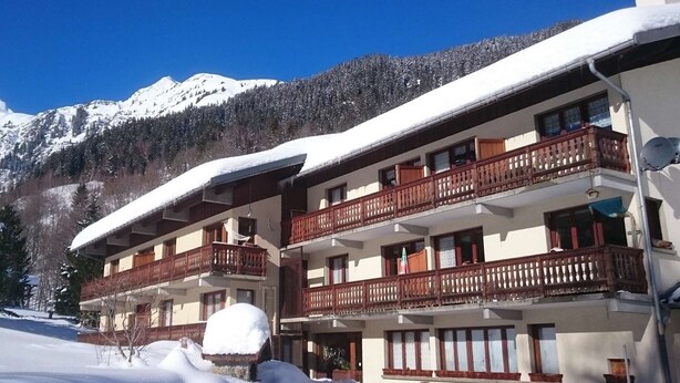A multi-story hotel with balconies, snow-covered surroundings, and a mountain backdrop.