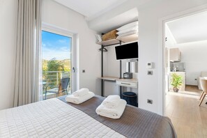 A hotel room with a bed, a desk, a TV, and a balcony with a view of the outdoors. - Frunze Luxury Apartments (Nafplio)