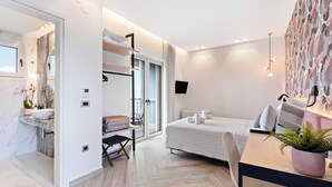 Quarto de hotel moderno com uma cama, escrivaninha, cadeira, planta, janela e banheiro com pia e espelho.