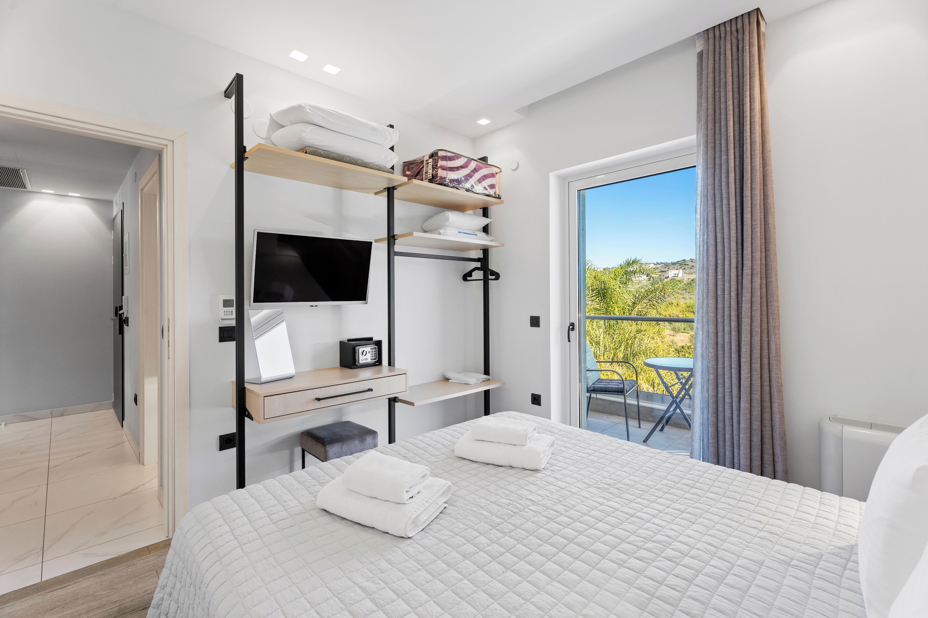 Une chambre d’hôtel moderne équipée d’un lit, d’une télévision, d’un bureau et d’un balcon avec vue.