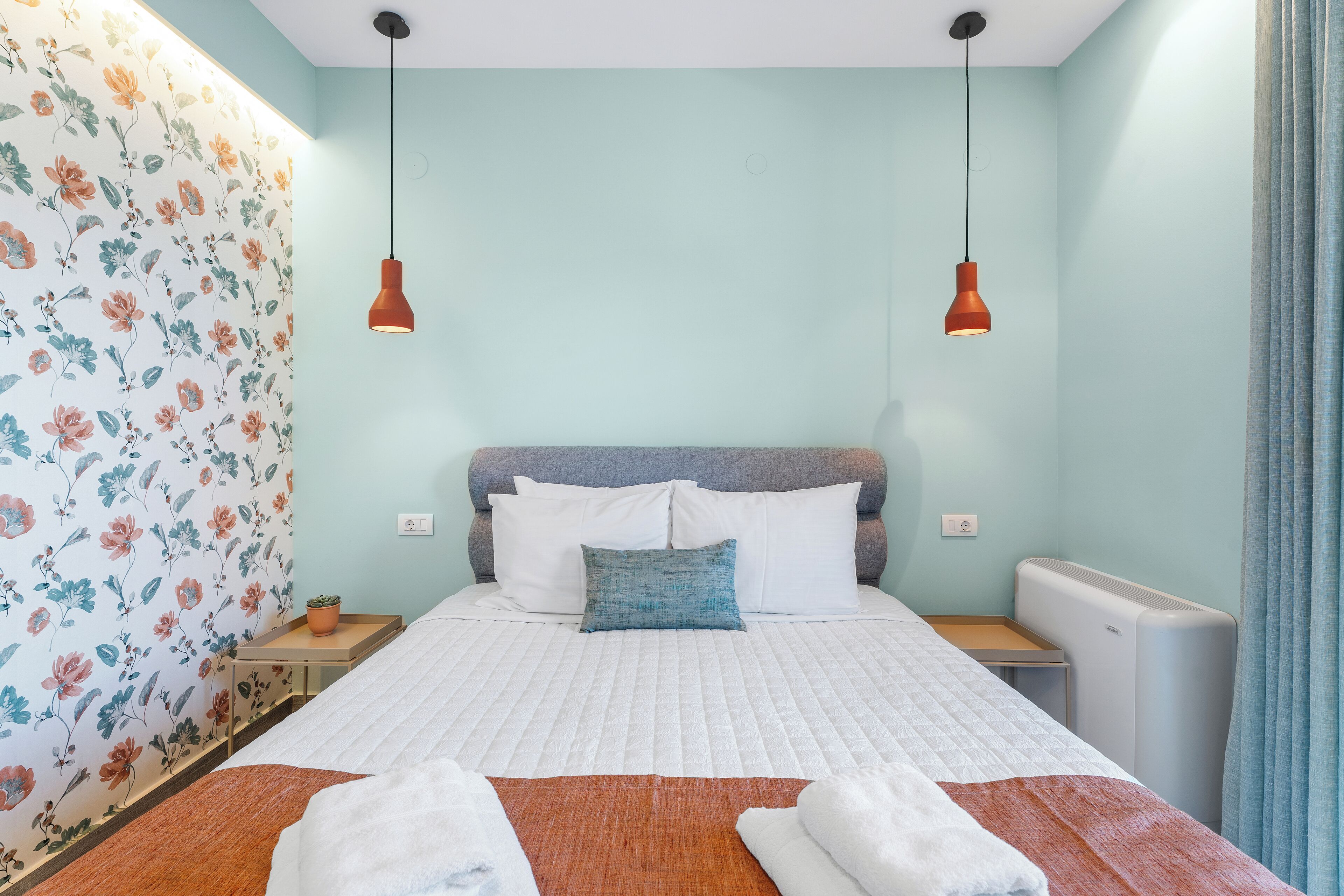 A neatly made bed with white bedding, a blue pillow, and two red pendant lights.