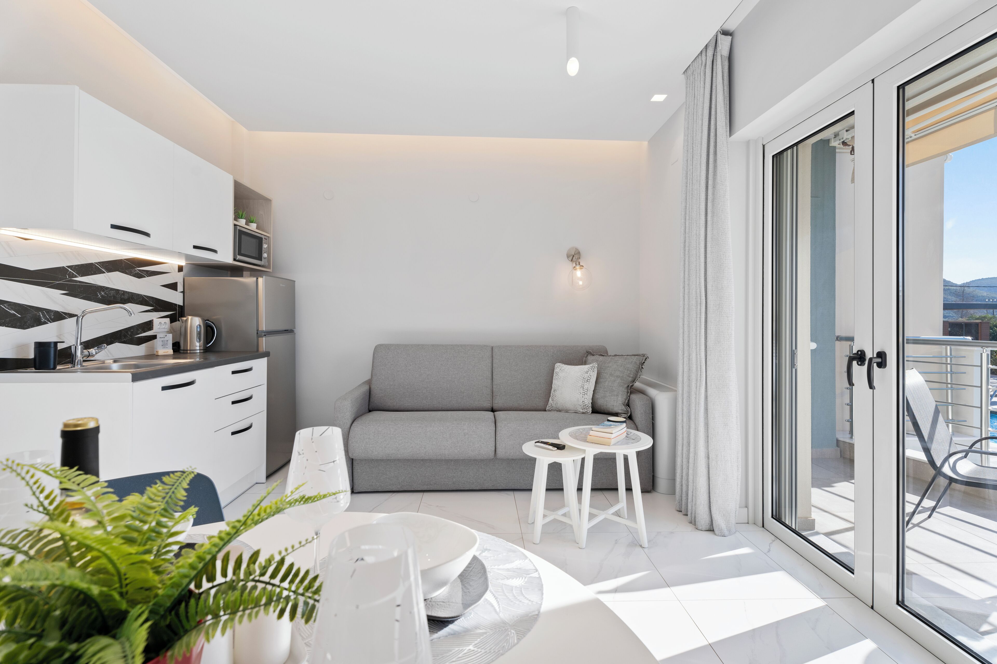 A modern kitchen with white cabinets, a grey sofa, and a dining area with a round table and chairs.