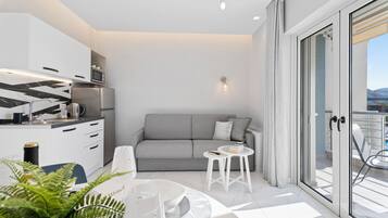A modern kitchen with white cabinets, a grey sofa, and a dining area with a round table and chairs.