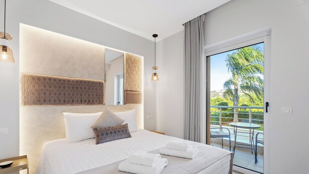 Quarto de hotel moderno com uma cama grande, varanda com vista para palmeiras e teto bem iluminado.