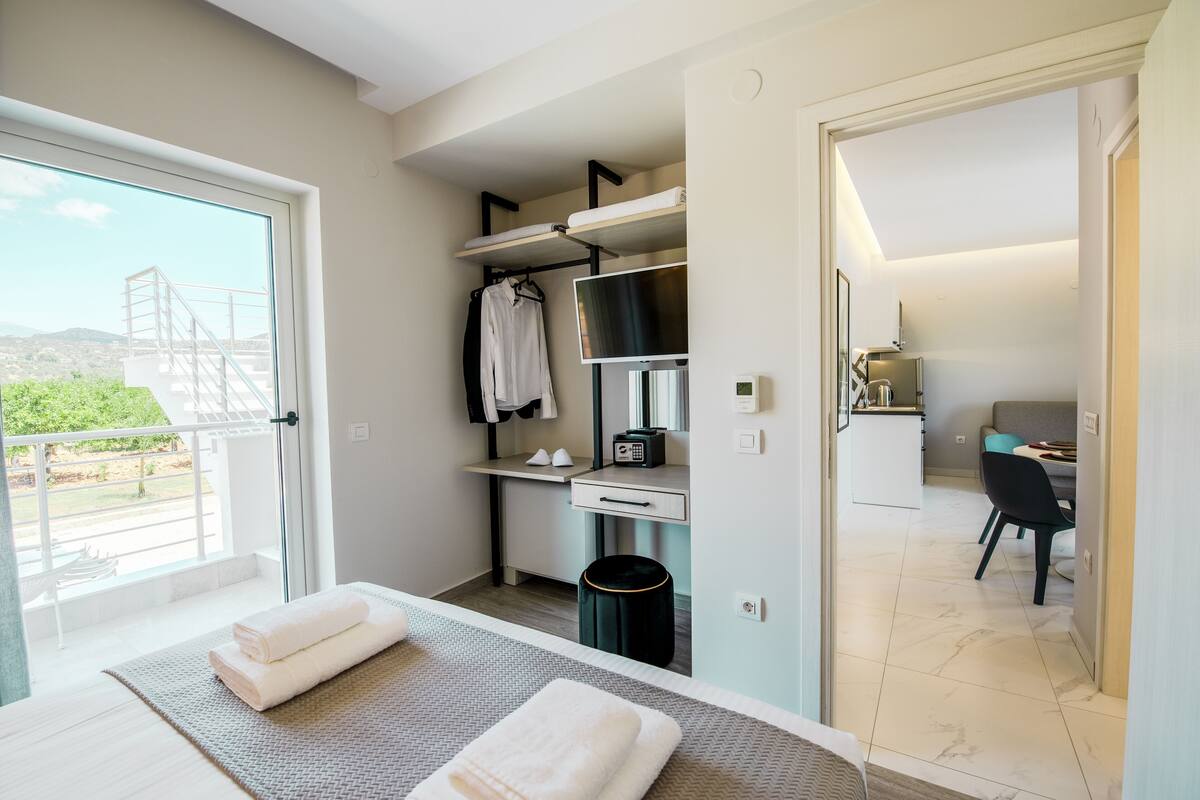 A modern hotel room with a balcony, a desk, and a dining area.