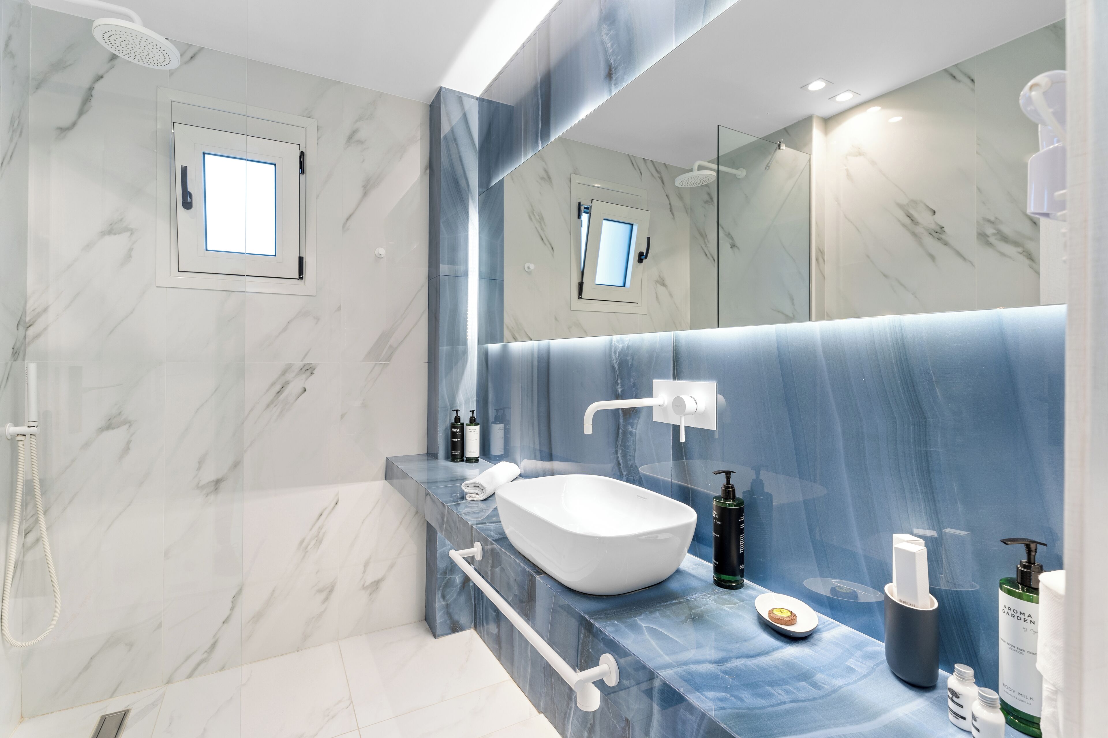 Une salle de bain moderne avec un lavabo blanc, des murs en marbre et un grand miroir.