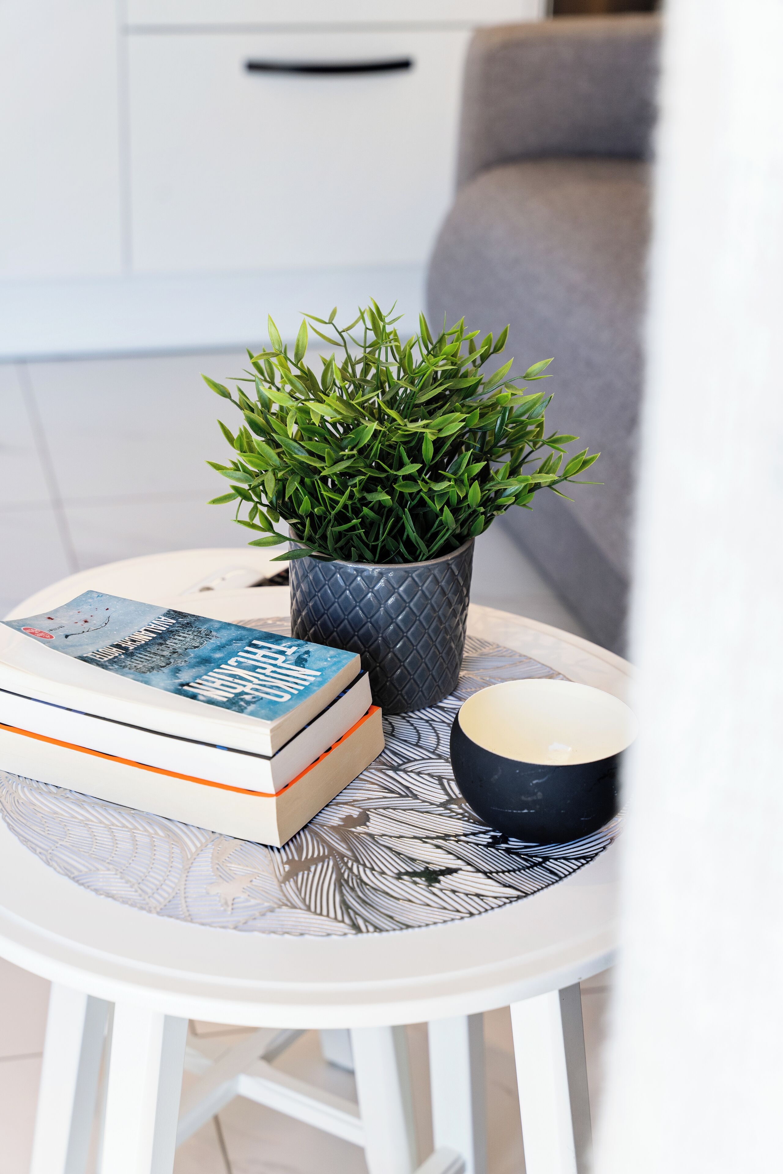A small round table with a potted plant, a stack of books, and a black candle.