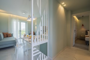A modern living room with a sofa, dining table, and staircase. - Frunze Luxury Apartments (Nafplio)