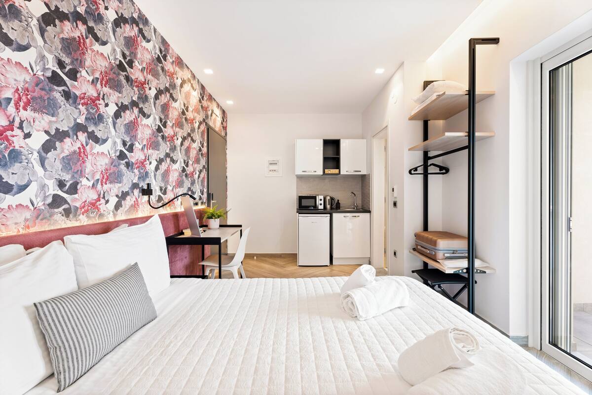 A hotel room with a bed, a desk, a kitchenette, and a bathroom.
