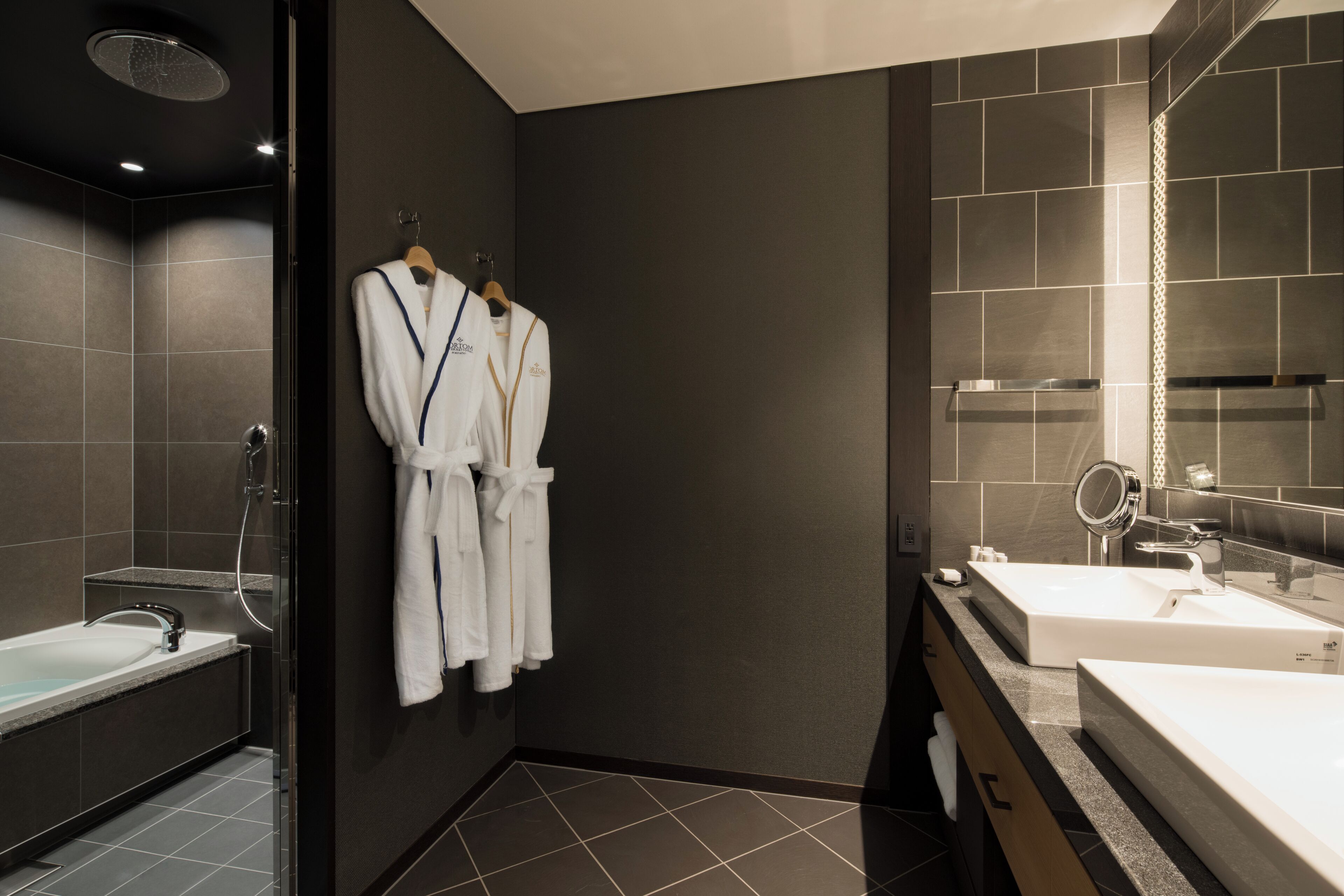 Une salle de bain moderne avec une douche à l’italienne, un meuble-lavabo double et un peignoir accroché au mur.