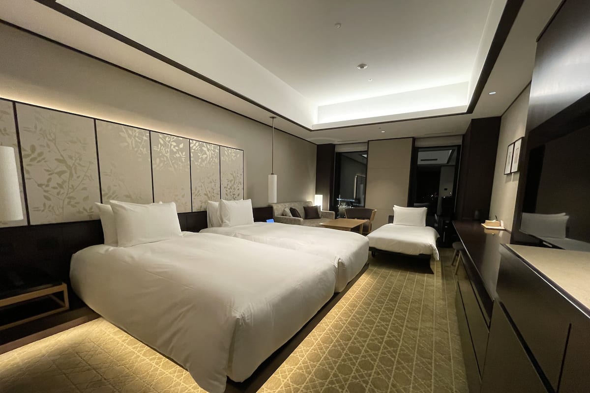 Ein Hotelzimmer mit zwei Betten, einem Schreibtisch, einem Sessel und einem großen Spiegel.
