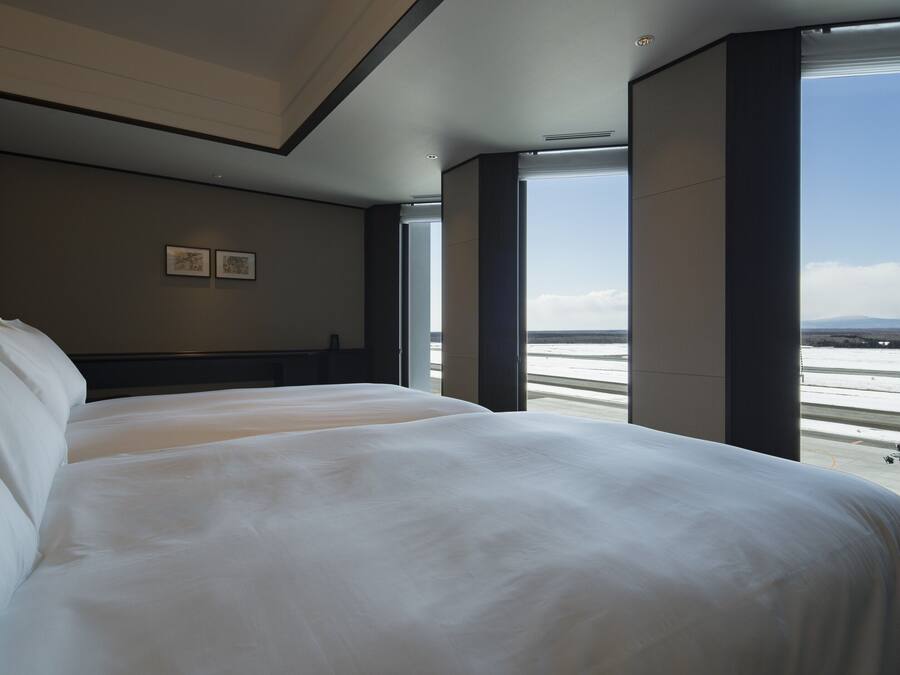 A hotel room with two beds, a large window, and a view of a snowy landscape.