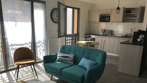 A modern living room with a teal sofa, a small white table, and a chair. A kitchen with a microwave and cabinets is visible in the background. - Beautiful apartment Arcachon - the Port (Arcachon)
