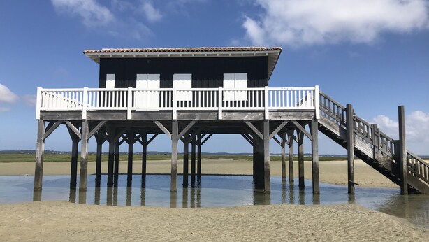 A wooden pier leading to a building with a balcony, situated on a sandy beach with calm water. - Beautiful apartment Arcachon - the Port (Arcachon)