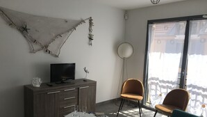 A modern living room with a TV on a wooden cabinet, a round floor lamp, and two chairs. - Beautiful apartment Arcachon - the Port (Arcachon)