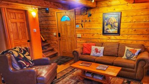 A cozy cabin interior with a leather armchair, a brown sofa with decorative pillows, a wooden coffee table, and a patterned rug.