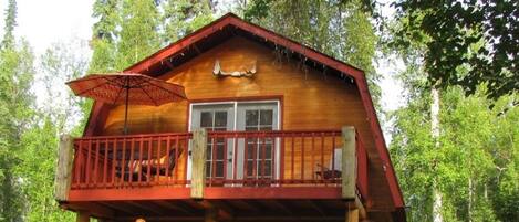Eine zweistöckige Blockhütte mit Balkon, umgeben von üppigem Grün.