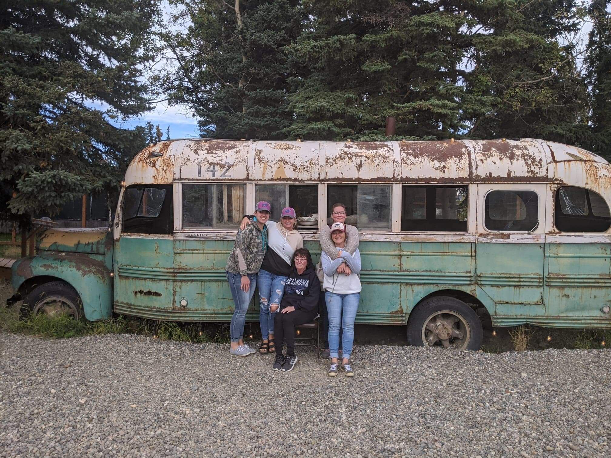 A group of people posing in front of a rusted, vintage bus with a visible number "142" on the side.