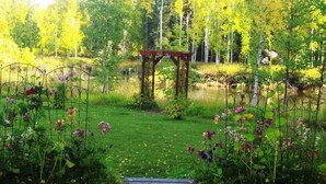 A garden with a wooden pergola, a pond, and various flowers.
