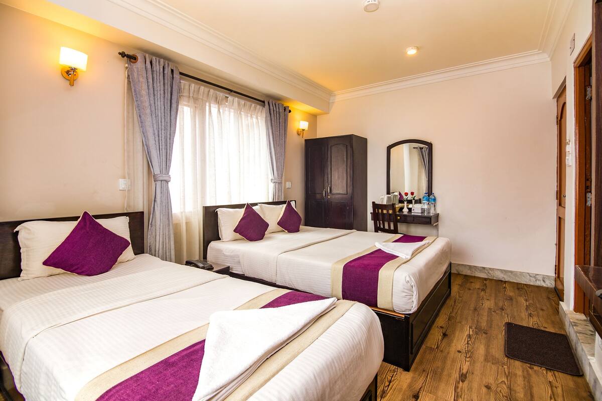 A hotel room with two beds, a wardrobe, a mirror, and a small table with toiletries.