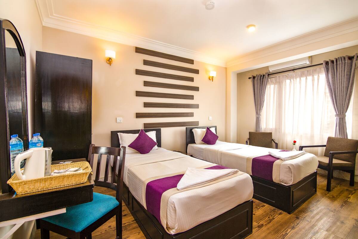 A hotel room with two beds, a desk with a basket, a chair, and a large mirror.