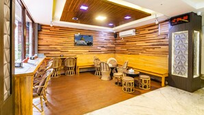 A room with wooden panel walls, a wooden reception desk, wicker chairs, a massage table, and a digital clock. - Hotel Livin Kathmandu (Kathmandu)