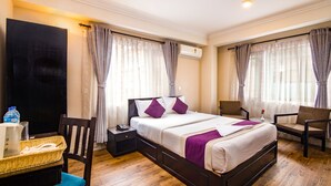 A hotel room with a bed, two chairs, a desk with a computer, a nightstand, and an air conditioning unit. - Hotel Livin Kathmandu (Kathmandu)