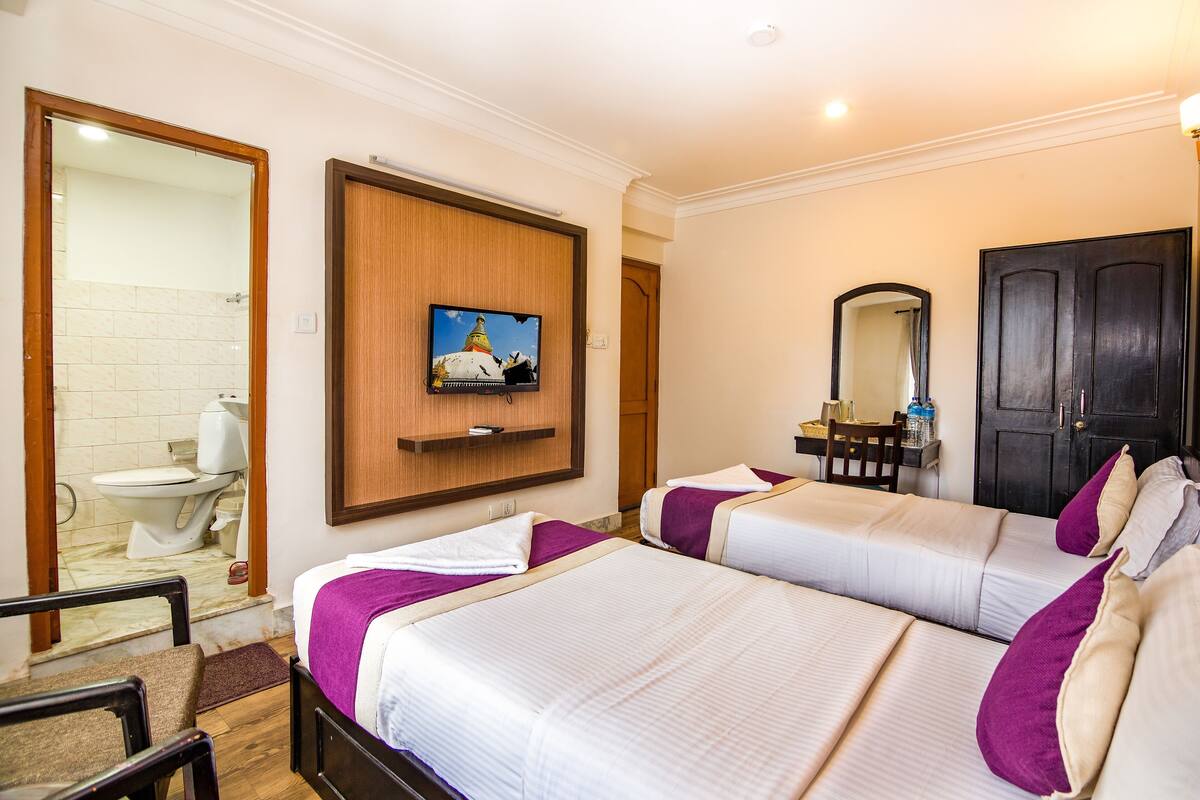 A hotel room with two beds, a TV, a mirror, and a bathroom visible through an open door.