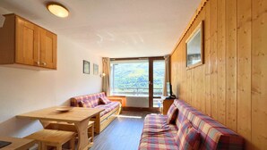 A cozy cabin interior with a wooden dining table, benches, a sofa, and a large window offering a scenic view. - Studio for 4 in Ménuires, renovated, mountain view (Les Menuires)