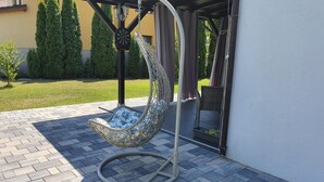 A hanging chair with a cushion on a patio. - Green Wood Residence (Ghiroda)