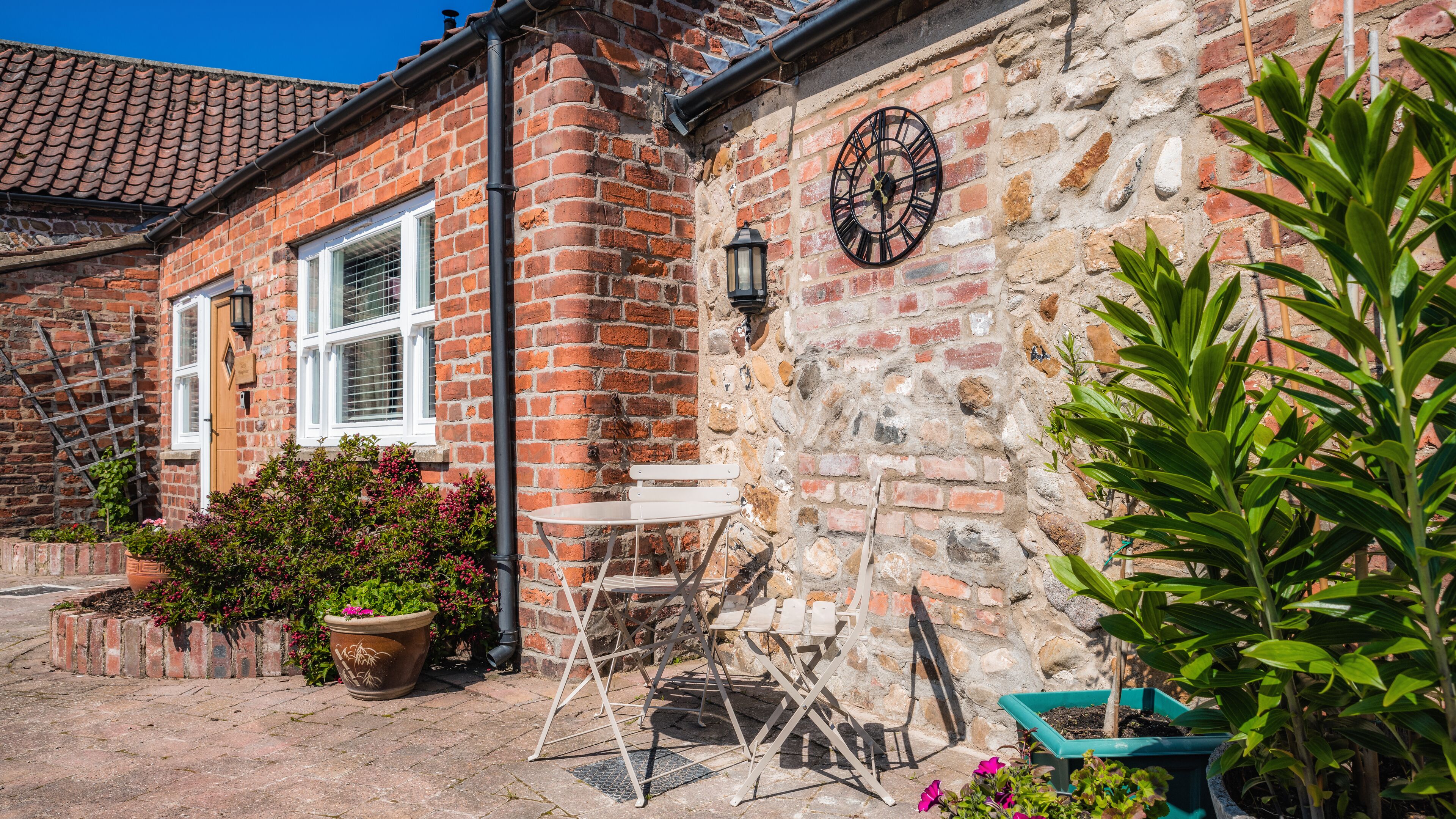 A brick house with a stone wall, a clock, and outdoor seating.