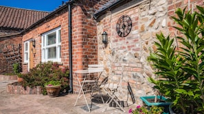 A brick house with a stone wall, a clock, and outdoor seating. - Village Farm Cottages.  (Driffield)