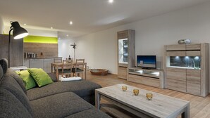Una sala de estar moderna con sofá, mesa de comedor, televisor y área de cocina.