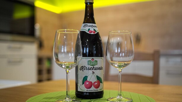 Una botella de Kirschwein sobre un tapete verde, con dos copas de vino vacías a su lado.