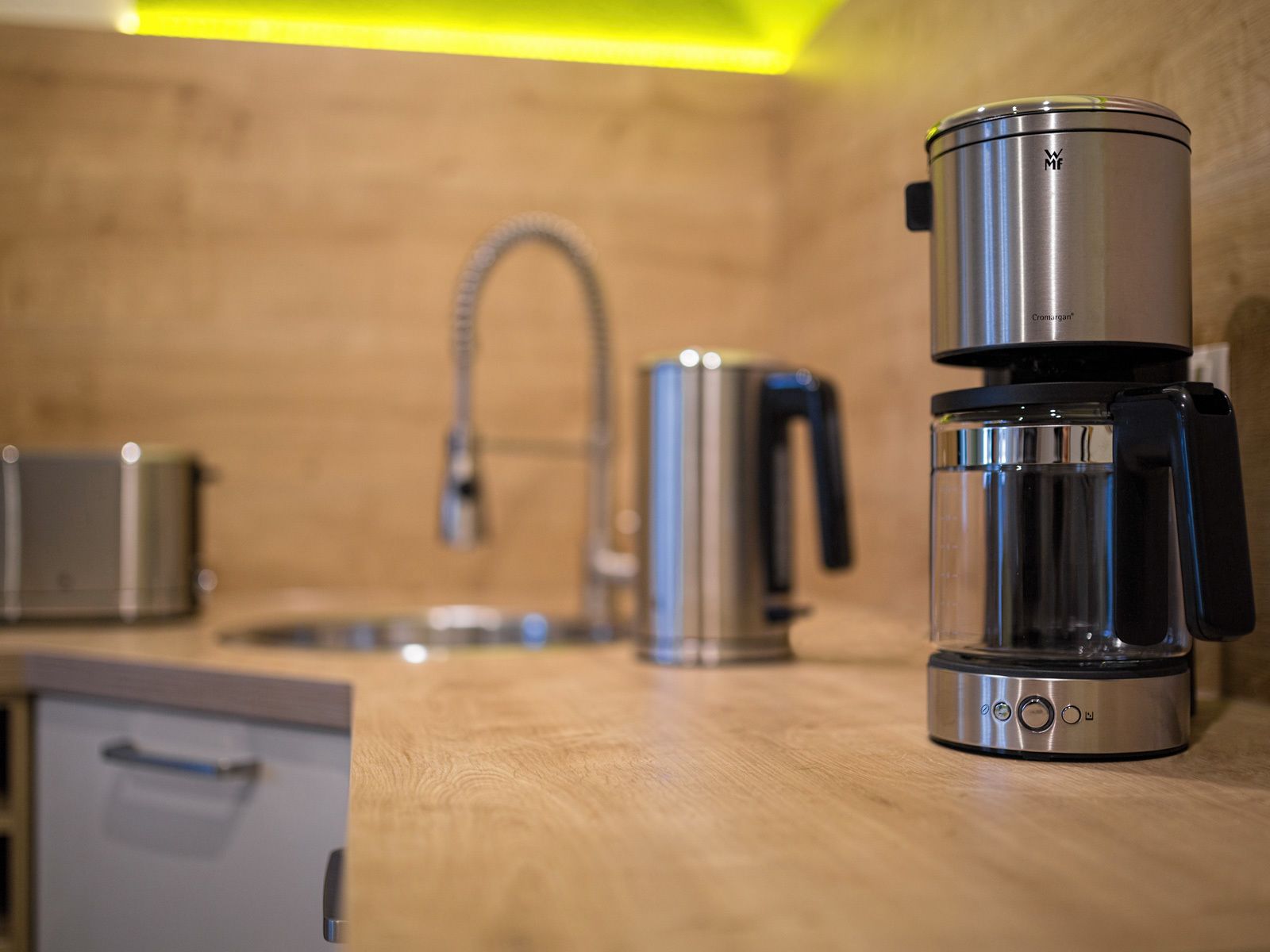 A kitchen with a coffee maker, a kettle, and a sink.