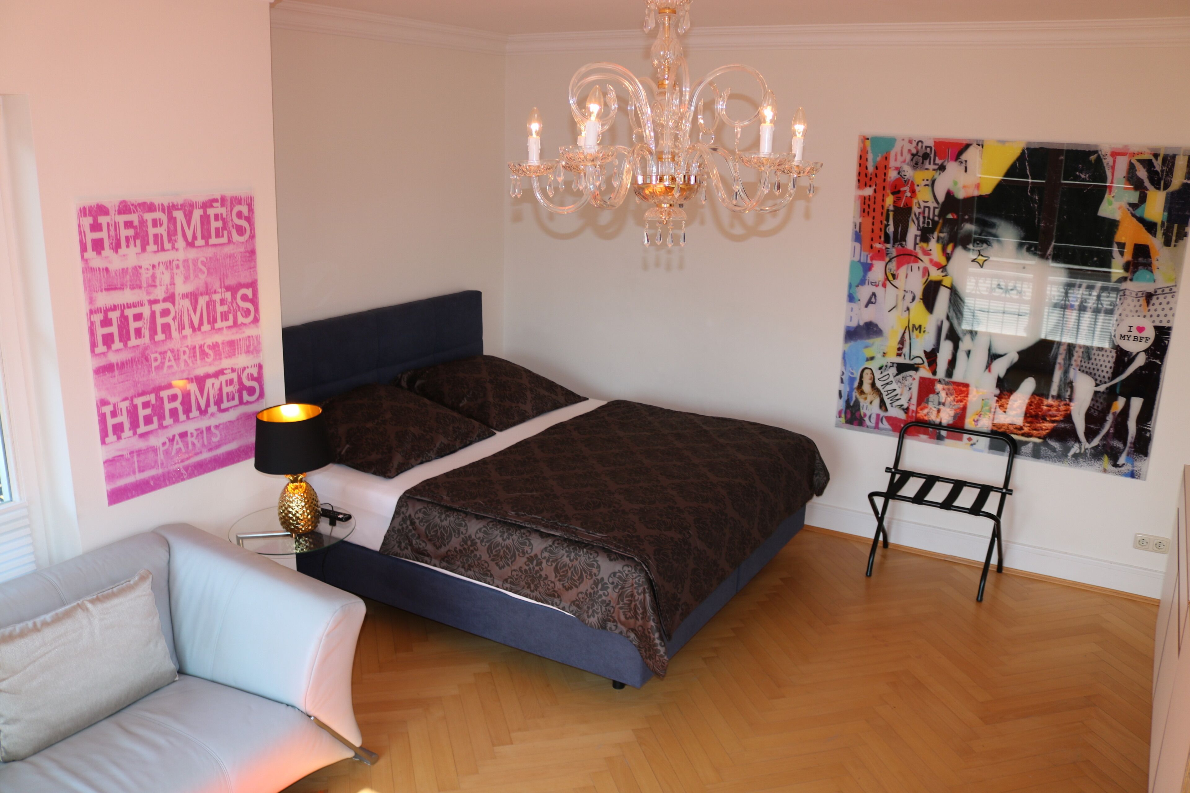 Une chambre à coucher avec un lit, un lustre, une œuvre d’art murale et une petite table avec une lampe.
