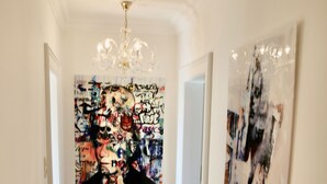 Ein Korridor mit Holzboden, einer Chandelüster und zwei Kunstwerken an den Wänden.