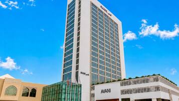 A tall, modern building with the name 'AVANI' on the facade, featuring a glass facade and a flat roof.