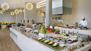 Zona de bufé con diversos alimentos y un cocinero preparándolos.
