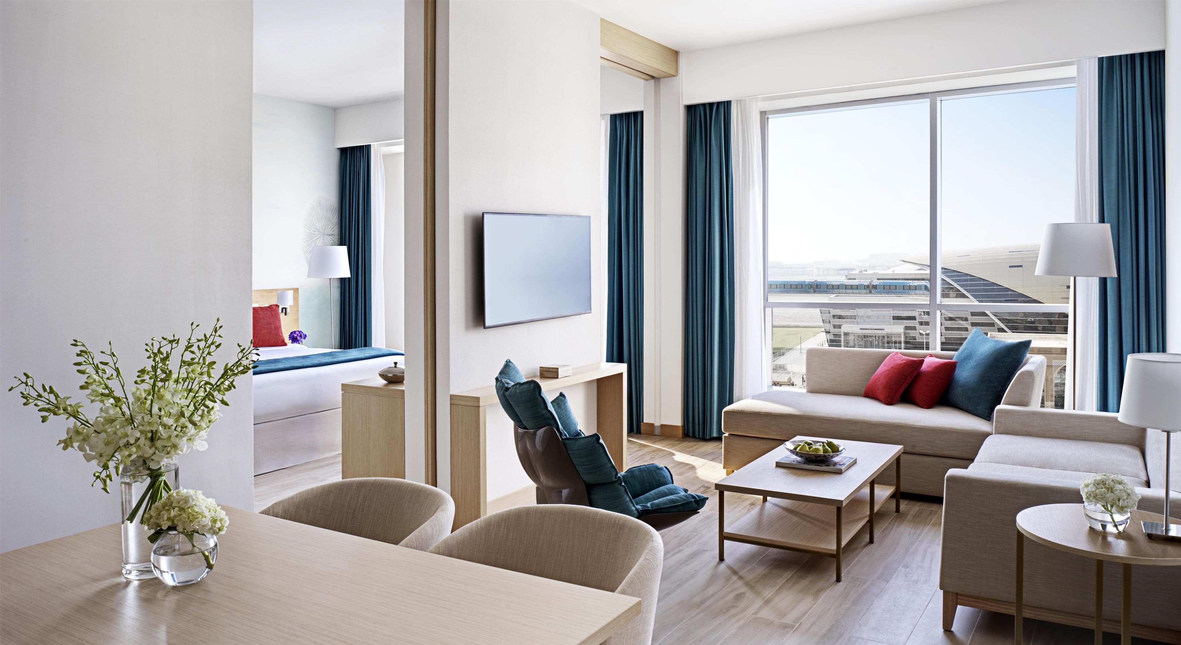 Quarto de hotel moderno com uma grande janela, um sofá, uma mesa de centro e um espaço de jantar.