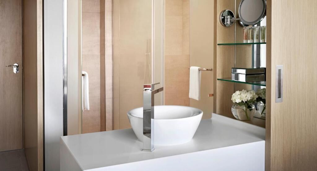 Een moderne badkamer met een witte wastafel, glazen planken en een spiegel.