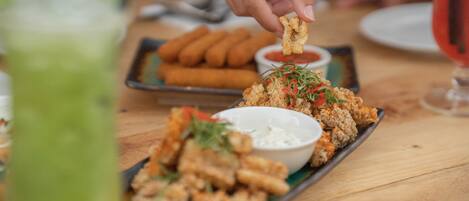 A tray of fried food with dipping sauce and a bowl of sauce on a wooden table.