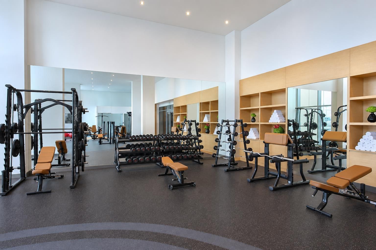 A gym with various exercise equipment, mirrors, and benches.
